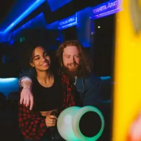 A happy couple enjoys a fun time playing a video game at a vibrant arcade setting.